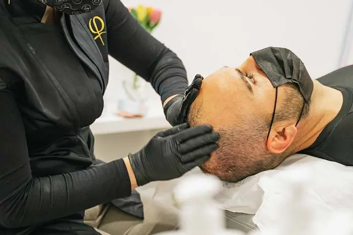 Helena Sas masajeando el cuero cabelludo de un hombre durante un tratamiento capilar profesional